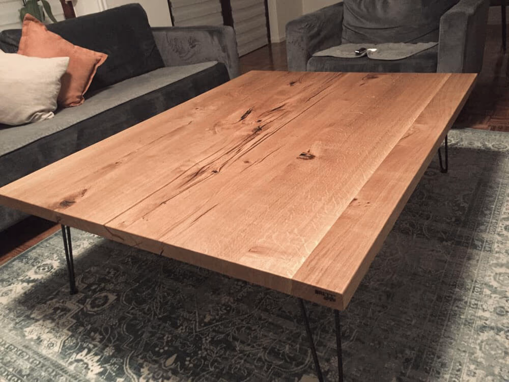 Couchtisch aus Massivholz mit markanter Maserung auf schwarzen Haarnadelbeinen in einem Wohnzimmer